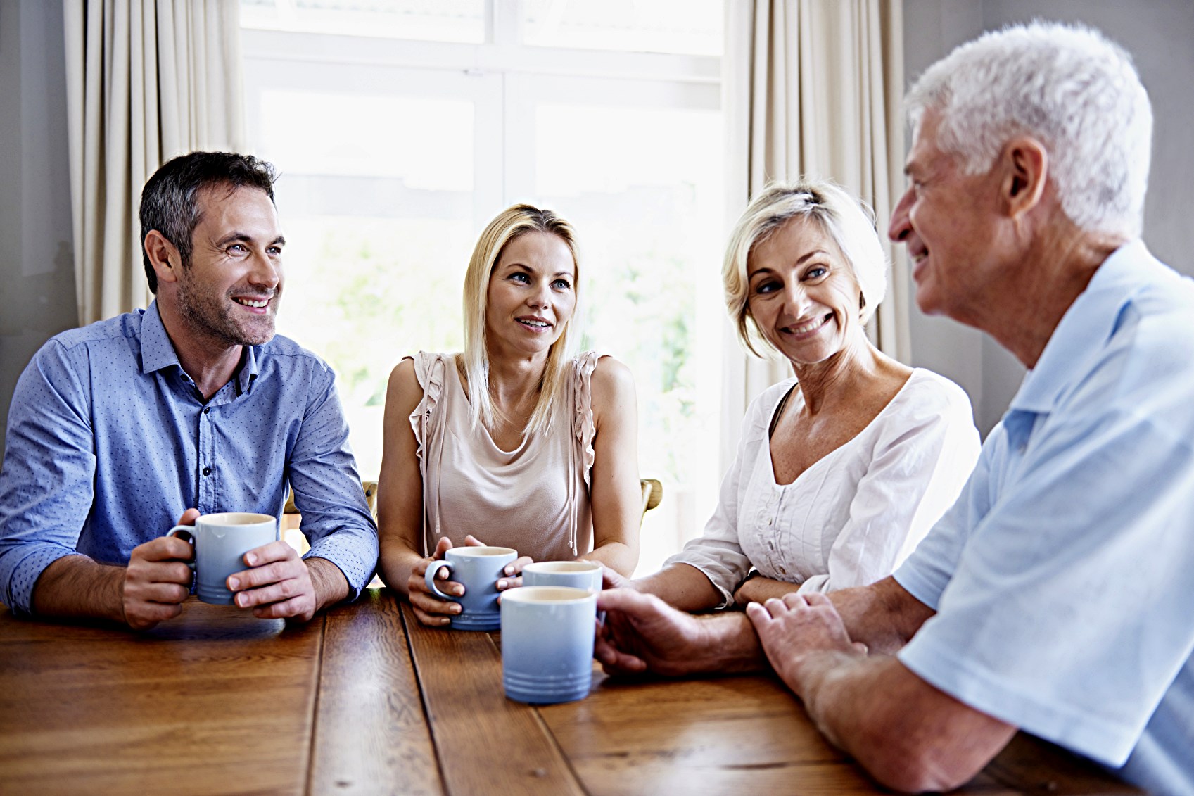 Shot of a young couple drinking coffee with their parents while sitting at a table at home